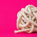 A loosely knotted ball of thick white rope sits on the right side of a vivid hot pink background, with several frayed strands beginning to unravel. The large area of empty space on the left creates a minimalist composition, suggesting the slow process of untangling a complicated relationship.